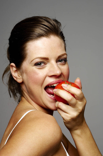 beautiful woman biting tomato - Fotó, kép