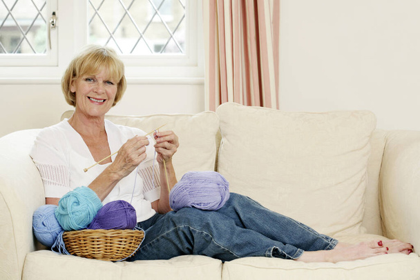 Senior woman sitting on the couch knitting - Fotoğraf, Görsel