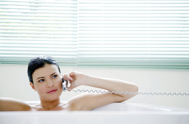 Woman talking on the mobile phone while sitting in the bathtub - Foto, Imagem