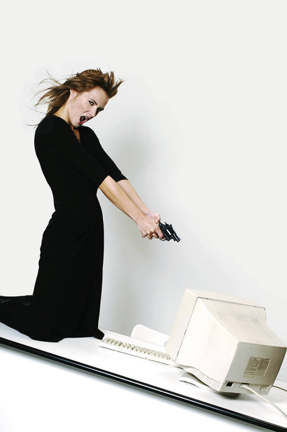 Businesswoman pointing her pistol at a computer monitor - Valokuva, kuva