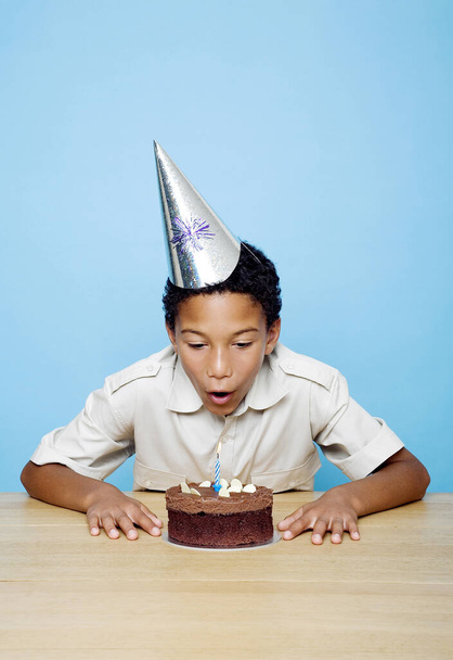 Menino com chapéu de festa soprando a vela em seu bolo de aniversário - Foto, Imagem