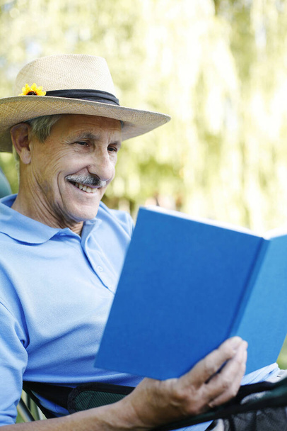 Senior man with hat reading book - 写真・画像