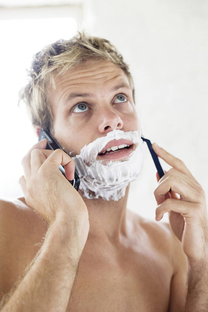 Bare chested man shaving while talking on the mobile phone - Foto, Imagen