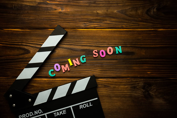 Coming soon Word made from multi-colored wooden letters on a brown wooden background and movie clapperboard. Filmmaking concept - Photo, image