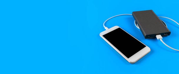 Top View smartphone nabíjení s power bank na modrém pozadí s kopírovacím prostorem. Nabíjení chytrého telefonu s napájecí bankou pomocí bílého USB kabelu. - Fotografie, Obrázek