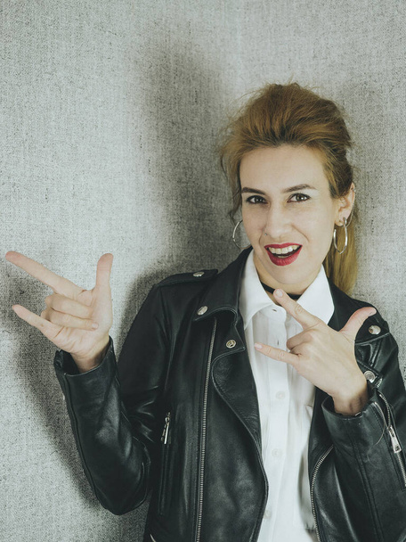 Beautiful girl in black leather jacket shows gesture rock - Foto, imagen