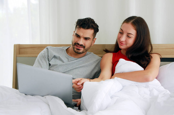 Kaukasisches Paar entspannt sich und arbeitet für das Online-Geschäft am Laptop in Social-Media-Technologie im Schlafzimmer. Arbeit von zu Hause aus und Lebensstil im Urlaub. - Foto, Bild