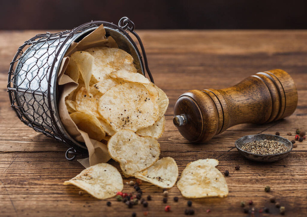 Potato crisps chips snack with black pepper snack bucket on dark wooden background with mill and ground pepper. - Фото, изображение
