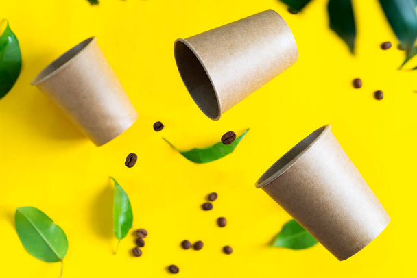Plovoucí ekologický papír jednorázové mockup poháry nad žlutým pozadím se zelenými palmovými listy. Nulový odpad - Fotografie, Obrázek