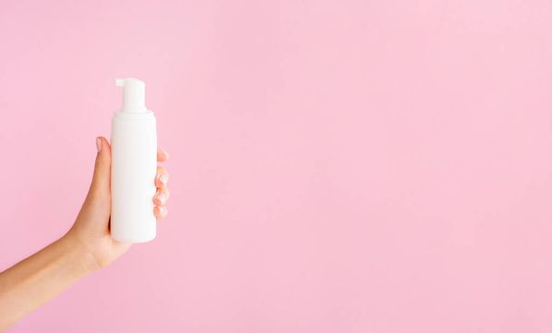 Reinigung kosmetischer Attrappen. Pumpflasche aus Kunststoff für Mousse oder Reinigungsschaum. Weibliche Hand hält weißes sauberes Glas mit Platz für das Logo. Pinkfarbener Hintergrund mit Kopierraum für Bannertext - Foto, Bild