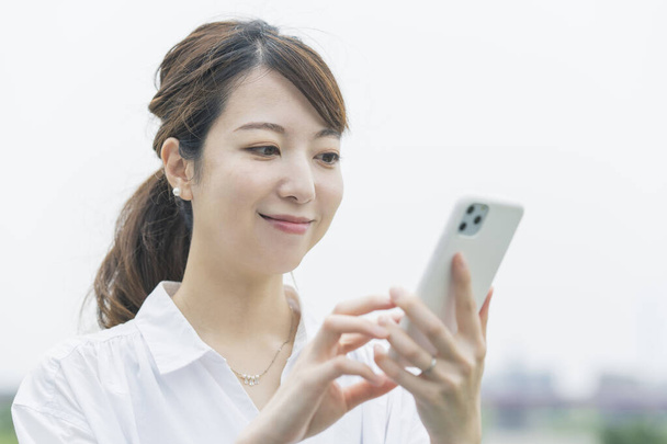 Mujer joven asiática operando mientras mira la pantalla del teléfono inteligente
 - Foto, imagen