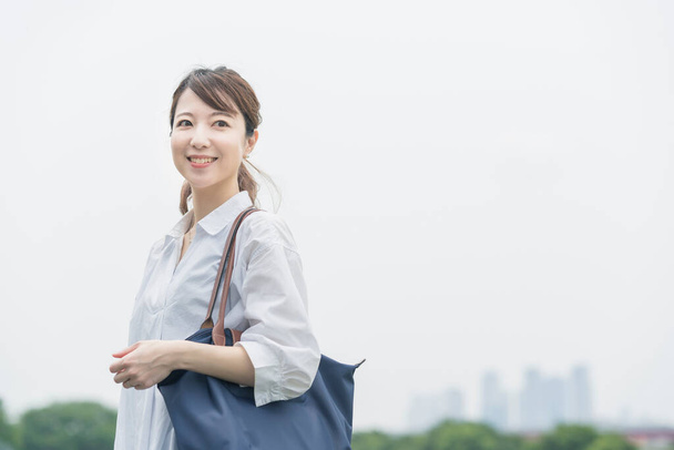 Asyalı bir kadın beyaz gömlek giyiyor ve rahatlatıcı bir atmosferde yürüyüş yapıyor. - Fotoğraf, Görsel