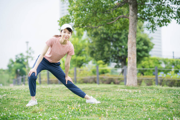 Asian young woman wearing sportswear and exercising in the park - Photo, Image