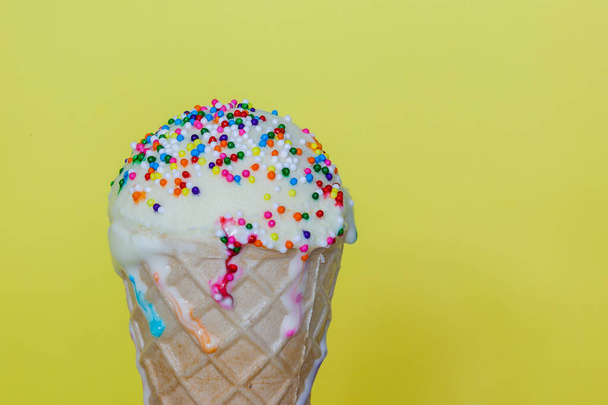 ワッフルコーンと黄色の背景に小さな虹色のスプリンクルを持つアイスクリーム - 写真・画像