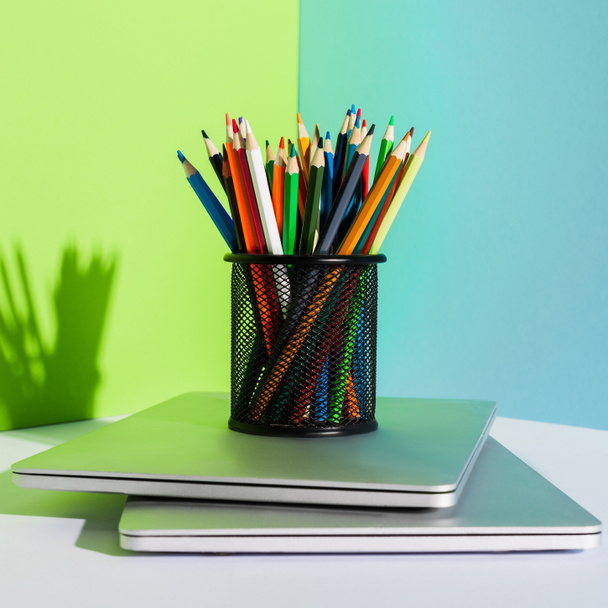 Bleistifthalter mit Buntstiften auf modernen Laptops auf blauem, grünem und weißem Hintergrund - Foto, Bild