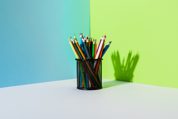 Potloodhouder met gekleurde potloden op blauwe, groene en witte ondergrond - Foto, afbeelding