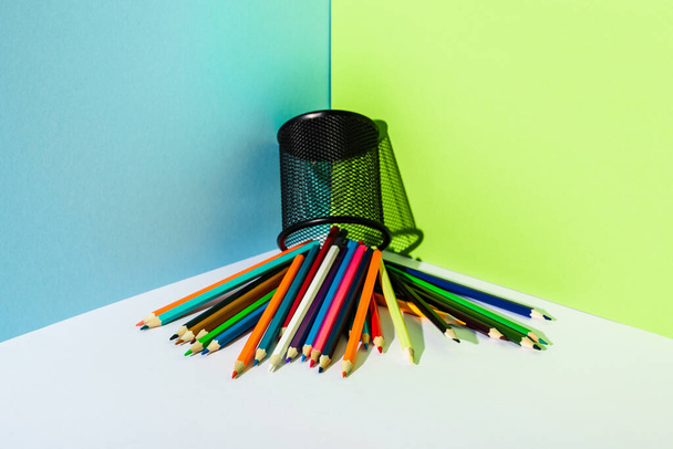 verspreide kleurpotloden van potloodhouder op blauwe, groene en witte ondergrond - Foto, afbeelding