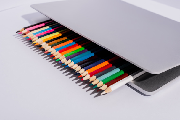 kolorowe ołówki w nowoczesnym laptopie na białym tle - Zdjęcie, obraz