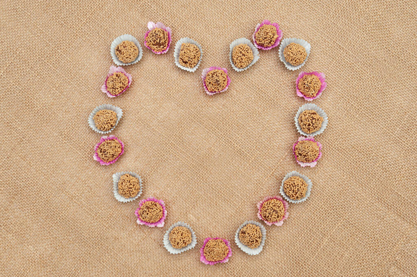 Traditional Brazilian candy called "Brigadeiro de Amendoim" in Brazilian Portuguese. Made with crushed peanuts, margarine and condensed milk. Top view. Heart shape. Copy space. Jute fabric background. - Photo, Image
