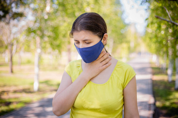 The girl in the mask holds his hand by the throat. Concept of sore throat and lack of fresh air during quarantine.   Copy space. - Photo, image
