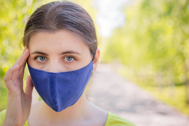 A young woman in a blue mask holds her head in her hands. The concept of headache and poor health due to self-isolation during the coronavirus pandemic.  Copy space.  - Fotoğraf, Görsel