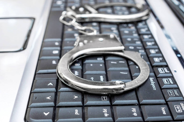 Handcuffs on the laptop's keyboard. Cyber crime concept. Close up. - Photo, Image