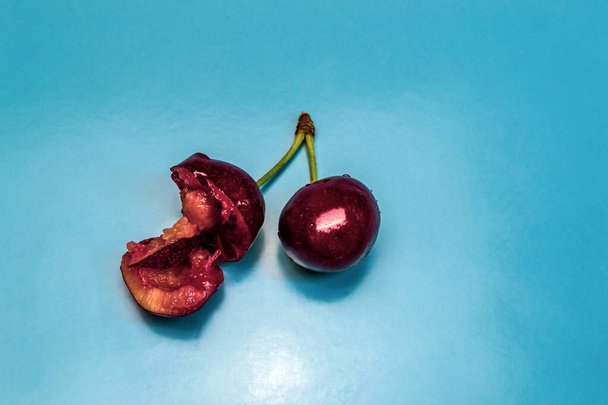 Due ciliegie rosse mature succose, una delle quali è morsa, sfondo blu - Foto, immagini