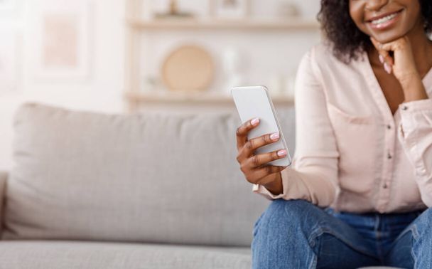 Matkaviestintä. Hymyilevä musta tyttö käyttää modernia älypuhelinta kotona, valikoiva Focus - Valokuva, kuva