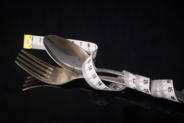 Koncept diety nebo hubnutí: vidlička a lžička s měřicí páskou omotanou kolem - Fotografie, Obrázek