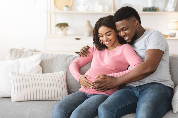 Lovely smiling expecting parents sitting on sofa at home - Fotó, kép
