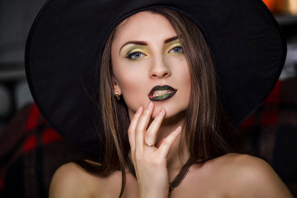 Portrait d'une belle jeune sorcière au maquillage vert avec un chapeau pointu noir. Studio photo, modèle avec peau propre, Halloween. - Photo, image