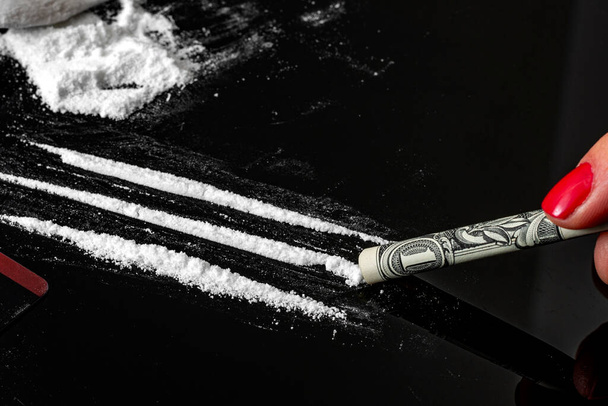 Uzależnienie od narkotyków i koncepcja nadużywania substancji z bliska na kłopotliwego narkomana za pomocą banknotu dolara jako słomki do wciągania linii kokainy na ciemnym lustrzanym stole obok stosu białego proszku - Zdjęcie, obraz