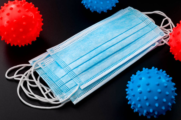 Pare a propagação da doença respiratória e medidas de proteção contra um conceito de surto pandêmico com máscara cirúrgica cercada por bolas vermelhas e azuis com picos como um coronavírus
 - Foto, Imagem