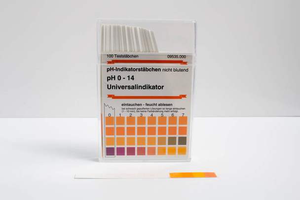 Fechar uma caixa de tiras de teste de indicador de pH sobre um fundo branco. Caixa de tradução: "100 tiras de teste. Fitas indicadoras de pH, não sangramento. Indicador universal de pH 0-14. Mergulhe - leia molhado
." - Foto, Imagem