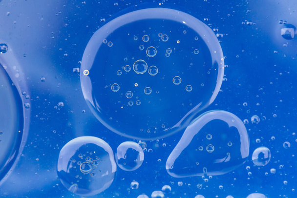 明るい青の背景を持つ水の中でグループ化された大規模な油泡. - 写真・画像