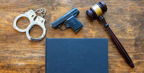 Hukuk, suç, ceza konsepti. Yargıç tokmak, tabanca, kelepçe ve ahşap masa arkasında boş bir kapak kitabı.. - Fotoğraf, Görsel