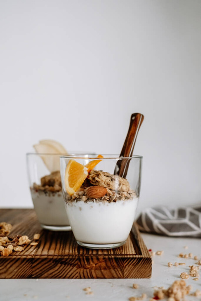 Muesli and natural yogurt with slices of fruits and nuts in a glass cup on a wooden board, healthy breakfast. High quality photo - Foto, imagen