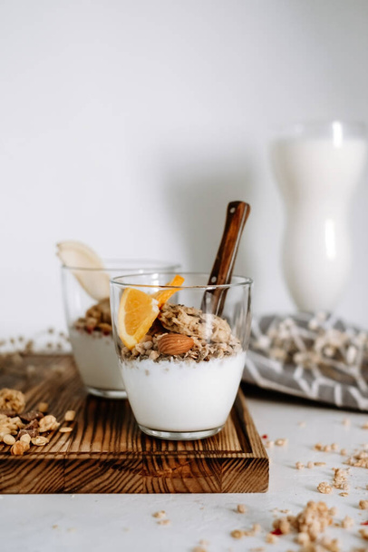 Muesli and natural yogurt with slices of fruits and nuts in a glass cup on a wooden board, healthy breakfast. High quality photo - Photo, Image