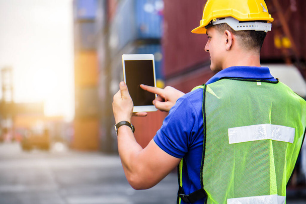 Young confident Caucasian man engineer using digital tablet and wearing yellow safety helmet and check for control loading containers box from Cargo freight ship for import and export, transport  - Zdjęcie, obraz