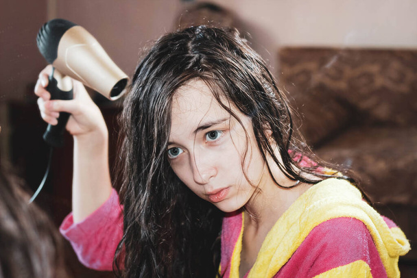 Портрет девочки-подростка, которая сушит волосы перед зеркалом феном. Крупный план, выборочный выстрел
. - Фото, изображение