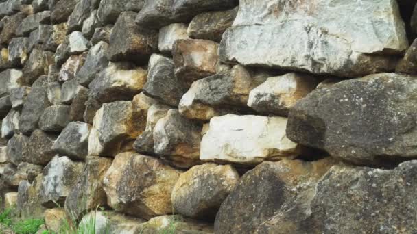 Kamenná zeď z přírodního tvrdého kamene. Hnědé a šedé zdivo venku ve starém parku podél travnaté stezky - Záběry, video
