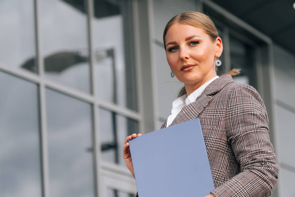 Stylish elegant woman of European appearance holds a folder with documents. The concept of a business lady against the background of the business center - Foto, immagini