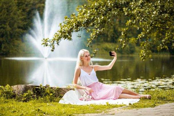 Full-length portret van een jonge vrouw rusten in de buurt van een vijver in een zomer park - Foto, afbeelding