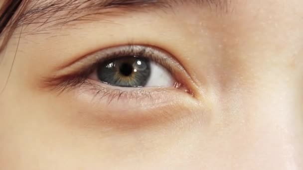 Een close-up van het blauwe oog van het meisje, dat water geeft door het felle licht. - Video