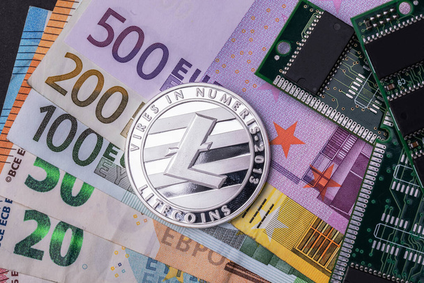 Ένα νόμισμα Litecoin κοντά στα μικροσχήματα, όλα τοποθετημένα σε διάφορα τραπεζογραμμάτια ευρώ. Άνω όψη. - Φωτογραφία, εικόνα