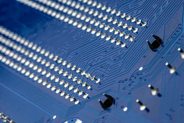 Macro photo of electrical paths on blue circuit board, visible soldering of the semiconductor tip. - Photo, Image