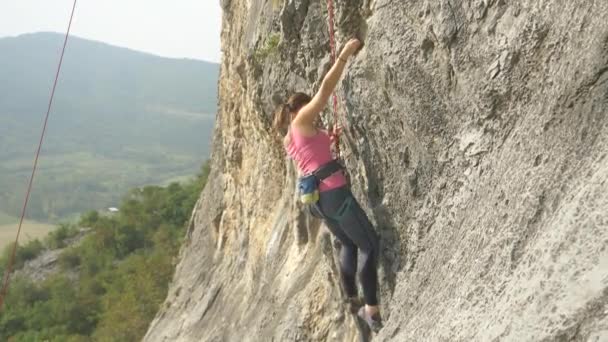 Ατρόμητη γυναίκα ορειβάτης σκαρφαλώνει σε ένα τεράστιο βράχο σε μια ηλιόλουστη καλοκαιρινή μέρα. - Πλάνα, βίντεο
