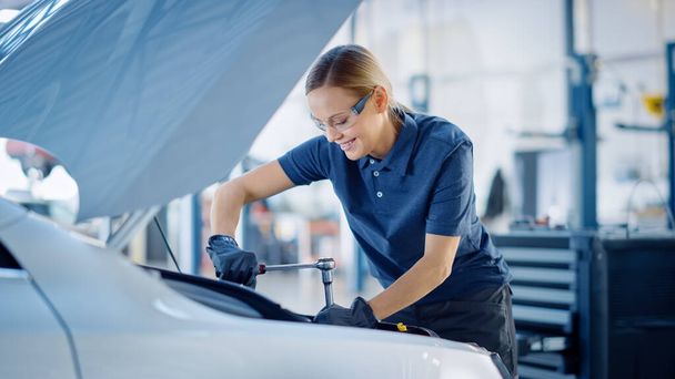 Güzel, güçlendirici kadın araba tamircisi serviste bir araç üzerinde çalışıyor. Ratchet kullanırken mutlu görünüyor. Uzman güvenlik gözlüğü takıyor.. - Fotoğraf, Görsel