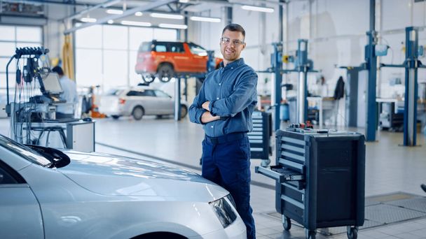 Handsome Car Mechanic is Posing in a Car Service. He Wears a Jeans Shirt and Safety Glasses. His Arms are Crossed. Specialist Looks at a Camera and Smiles. - Photo, Image