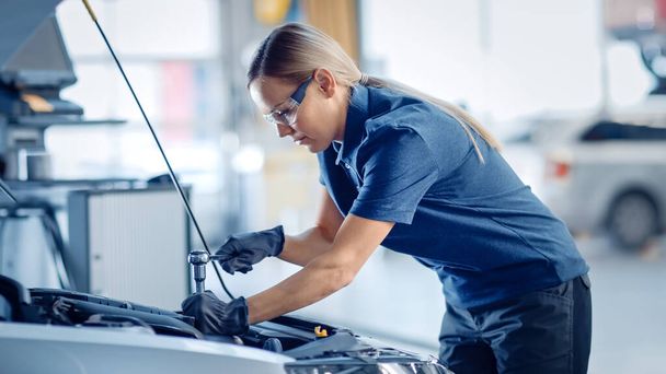 Krásná posilující ženské mechanik pracuje na autě v automobilové službě. Žena v bezpečnostních brýlích opravuje motor. Ona používá Ratchet. Moderní čistá dílna s vozidly. - Fotografie, Obrázek